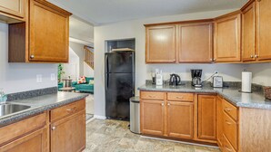 A kitchen with wooden cabinets, a black refrigerator, granite countertops, and a trash can. - Central Duplex Townhome Close to Twin Cities (St. Paul)