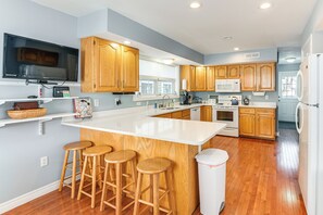Una cocina moderna con armarios de madera, una isla grande con taburetes, horno empotrado, microondas y refrigerador.