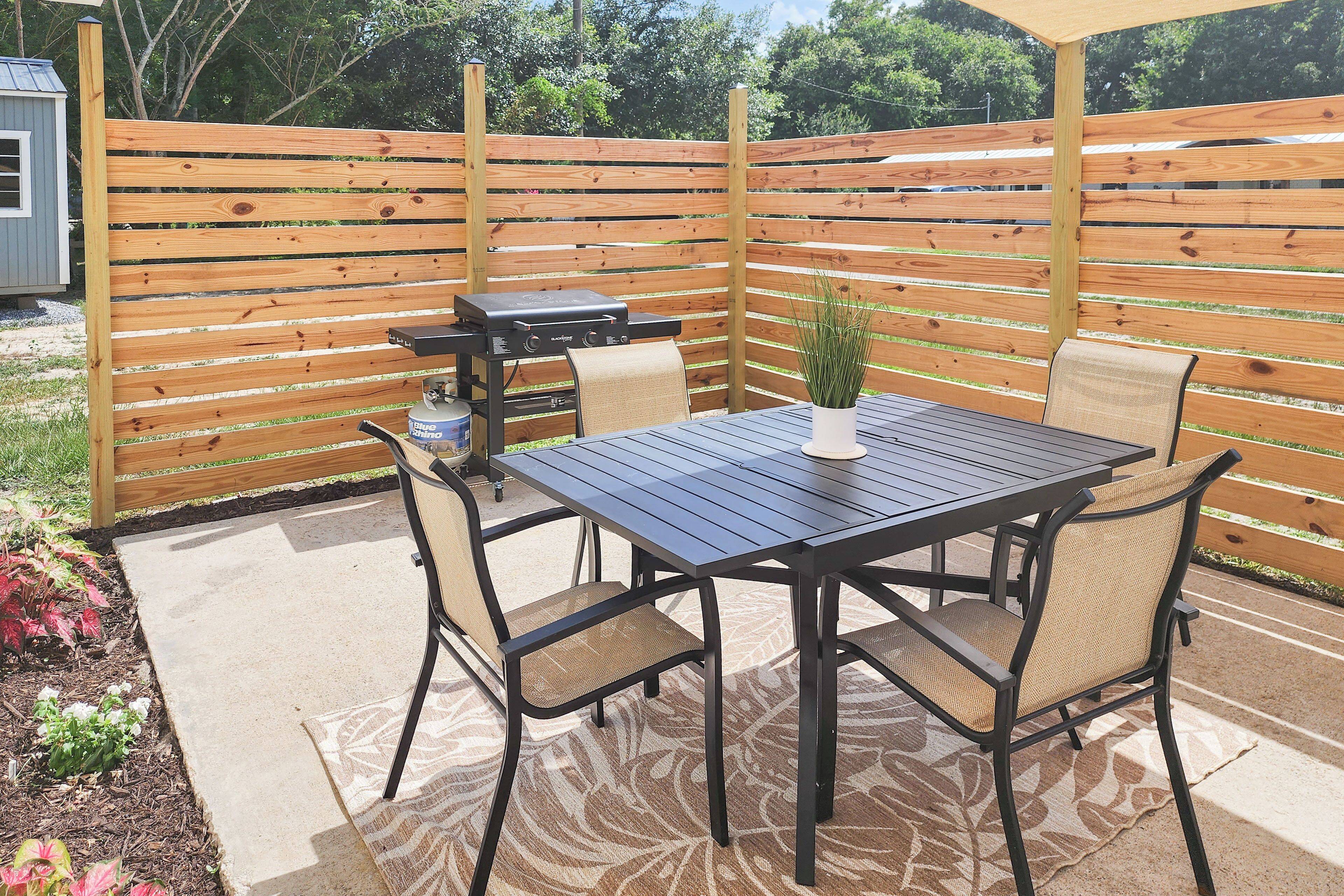 An outdoor patio with a table and chairs, a grill, and a wooden fence.