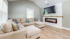 Una sala de estar con un sofá modular, una chimenea y un televisor montado.