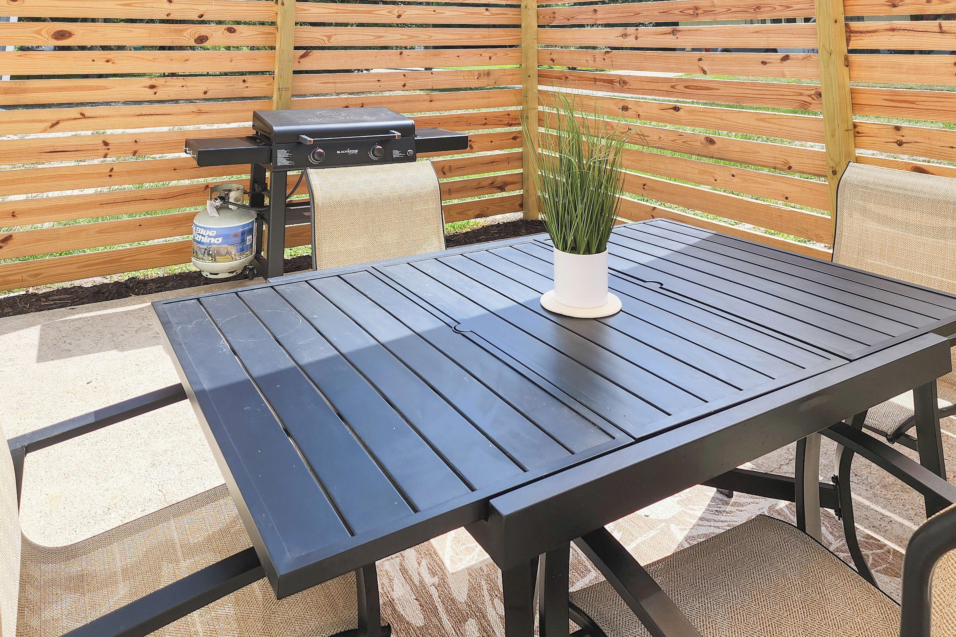 Un patio al aire libre con una mesa y sillas de metal negro, una parrilla y un tanque de gas.