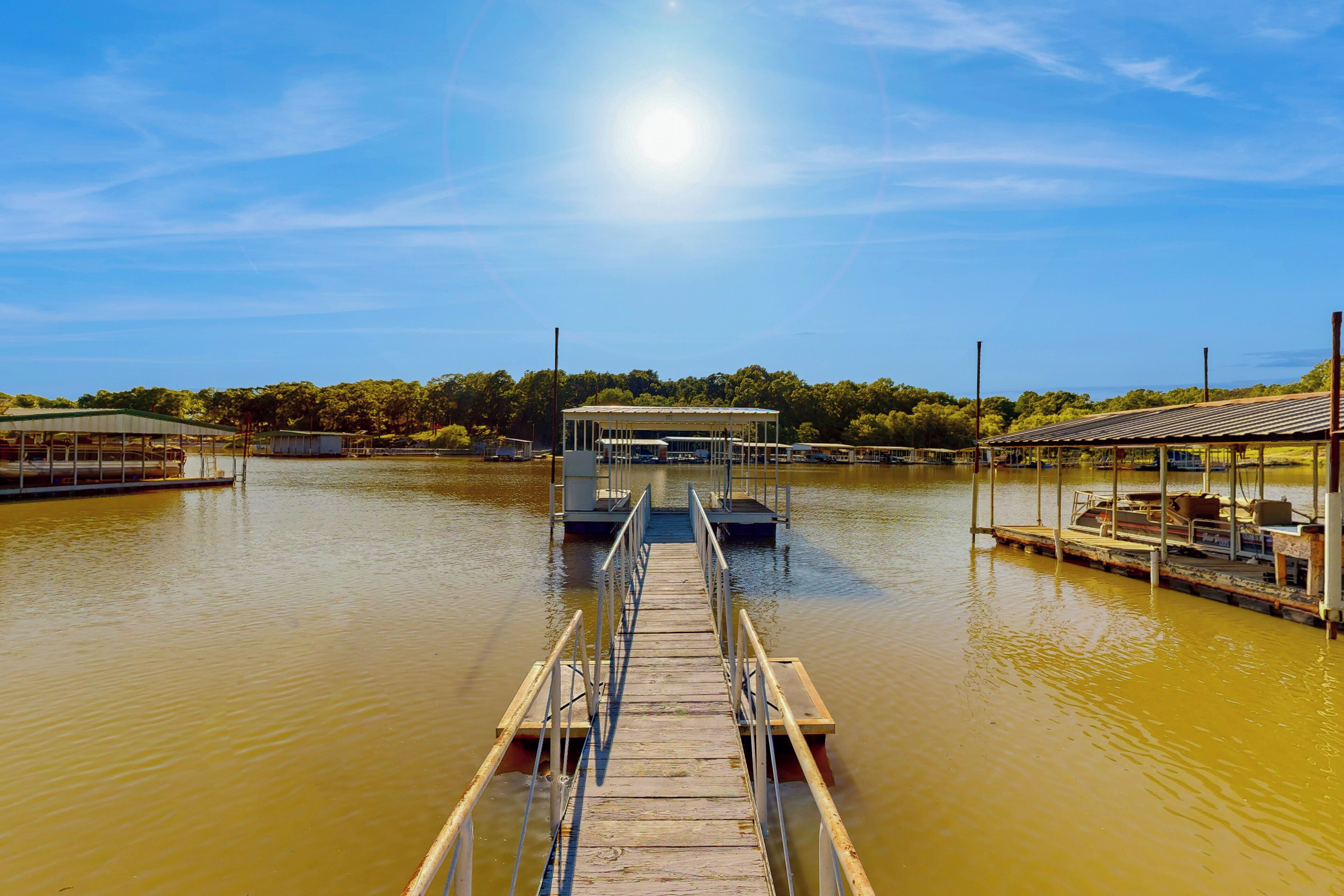 A wooden dock leading to a covered boat launch area with a clear sky and calm water.