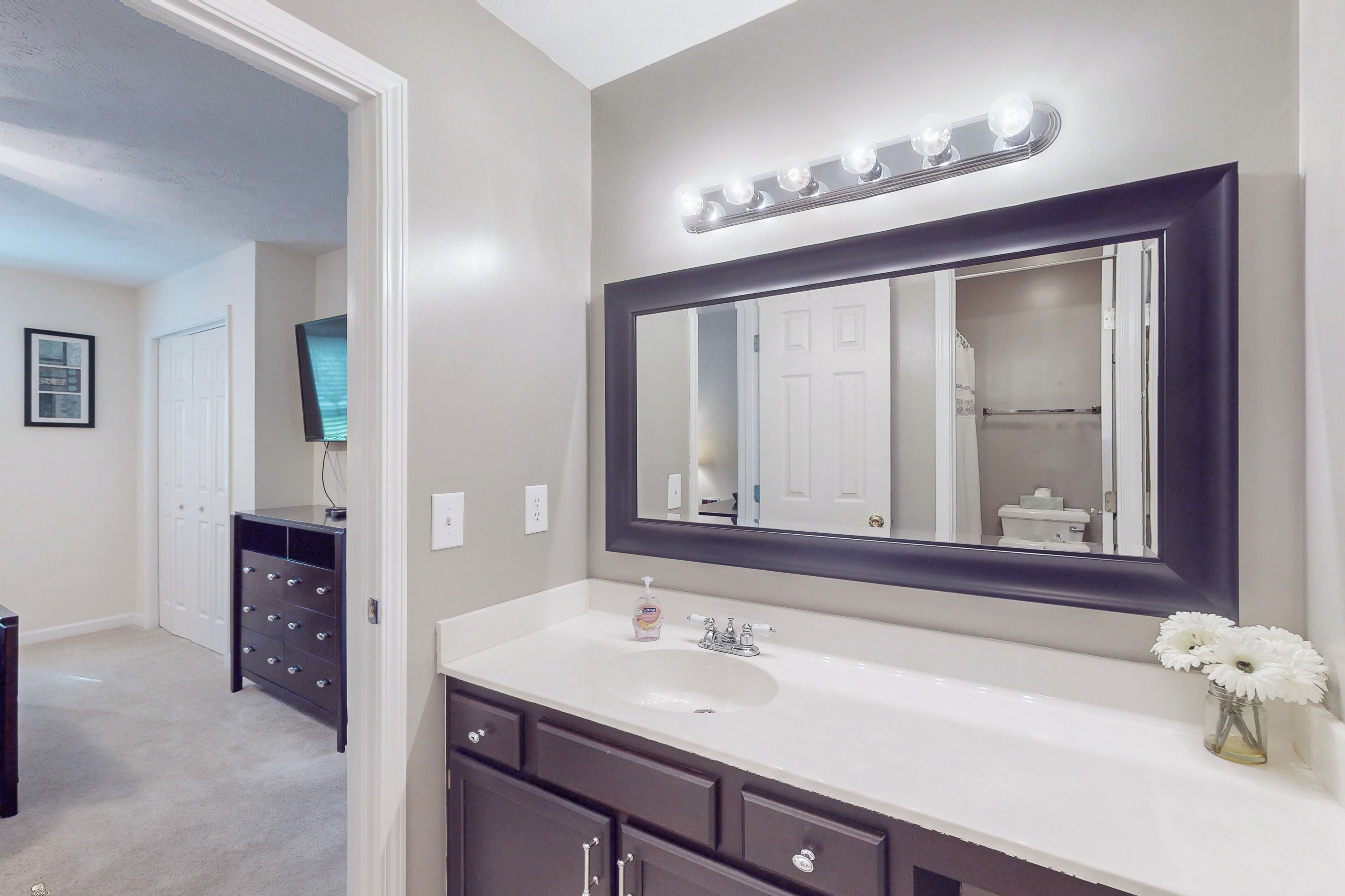 A bathroom with a large mirror, vanity, and a sink.