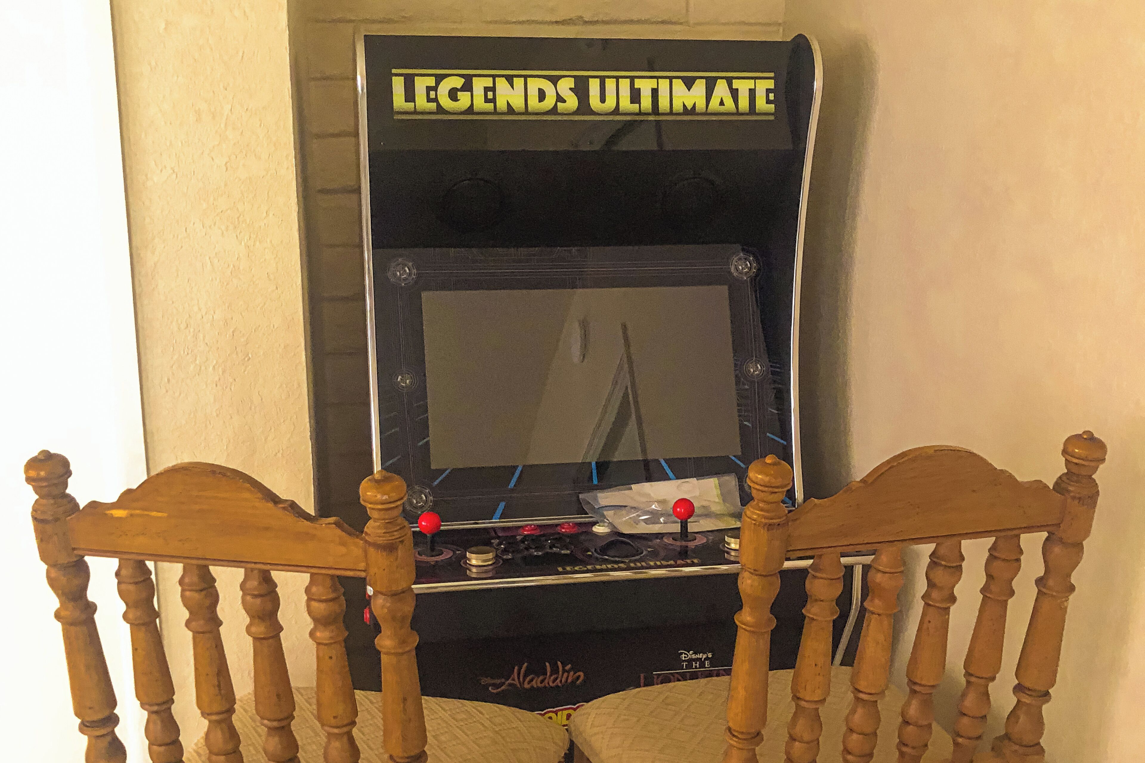 Una silla de madera con respaldo y reposabrazos frente a una consola de videojuegos que dice 'LEGENDS ULTIMATE'.