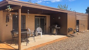 Un espace patio aménagé avec une table et des chaises, un barbecue et un coin salon abrité.