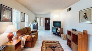Un salon avec un canapé, un téléviseur, un meuble en bois et un tapis.