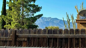 Une clôture en bois avec une antenne parabolique montée sur une structure en briques, un grand arbre et une chaîne de montagnes en arrière-plan.