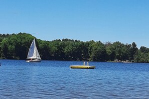 Un velero en un lago tranquilo con un muelle y una orilla boscosa al fondo.