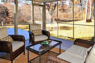 Un patio techado con mobiliario de mimbre, una mesa de vidrio y vistas a un área boscosa.