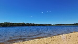 A beach with clear blue water, a sandy shore, and a forested area in the background. - Pool & Beach Access! 'lake Arrowhead Hideaway' (Nekoosa)