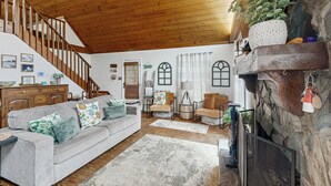 Un vaste salon agrémenté d’un escalier en bois, d’une cheminée en pierre et d’un coin salon confortable avec un canapé et des fauteuils.