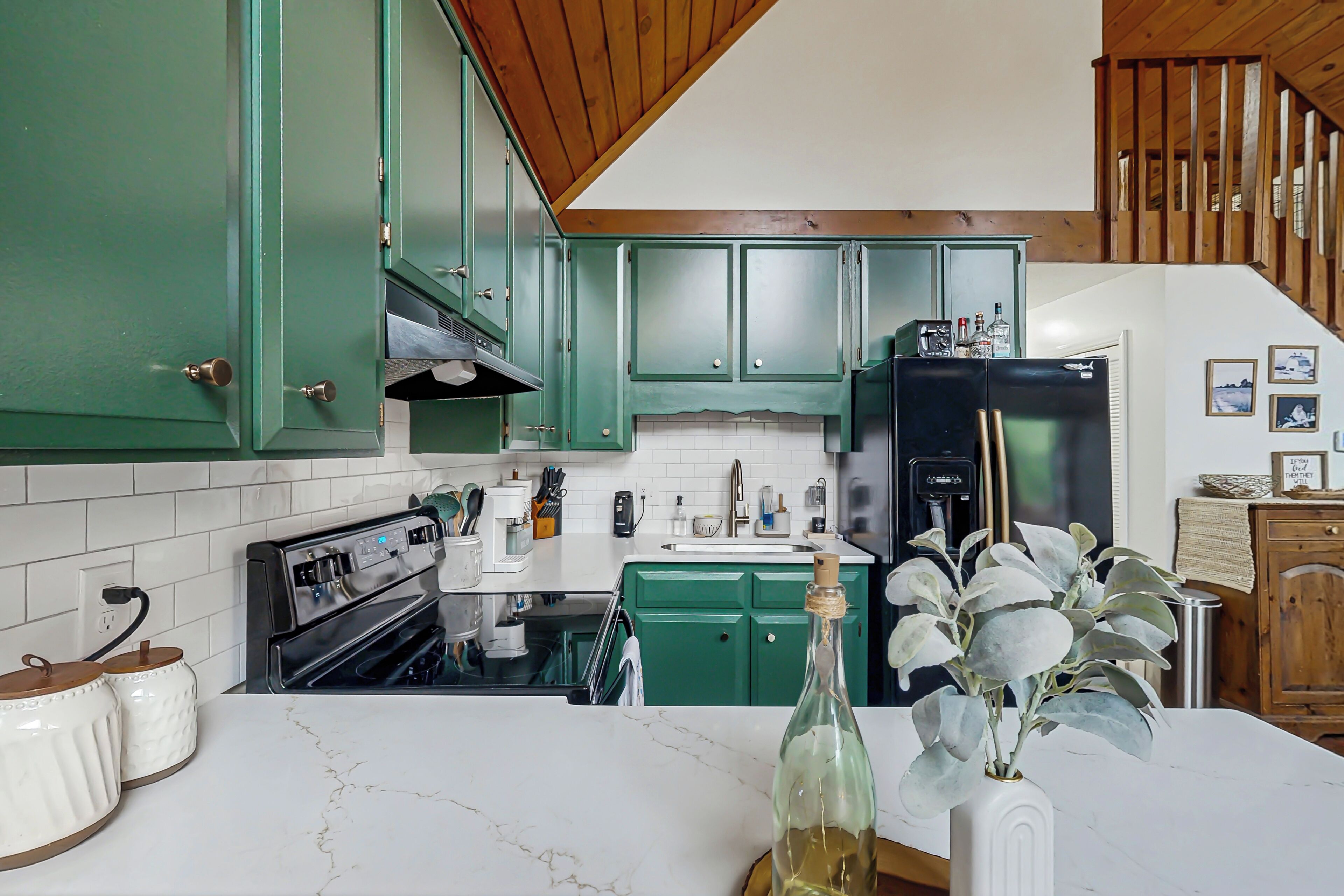 A kitchen with green cabinets, a black refrigerator, and a marble countertop.