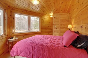 A wooden cabin room with a bed, a window, a lamp, and a small table. - Trails & Streams On-site: Wardensville Escape! (Wardensville)