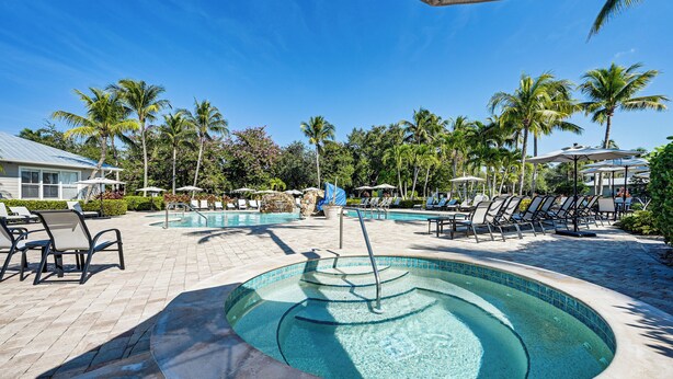 A pool area with lounge chairs and umbrellas, surrounded by palm trees and a clear blue sky. - Overlooking 10th Fairway 2 Free Rounds of Golf (Naples)