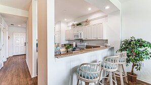 A kitchen with white cabinets, a microwave, and a bar area with wicker chairs. - Overlooking 10th Fairway 2 Free Rounds of Golf (Naples)