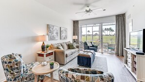 A spacious living room with a sofa, two patterned armchairs, a coffee table, and a television. - Overlooking 10th Fairway 2 Free Rounds of Golf (Naples)