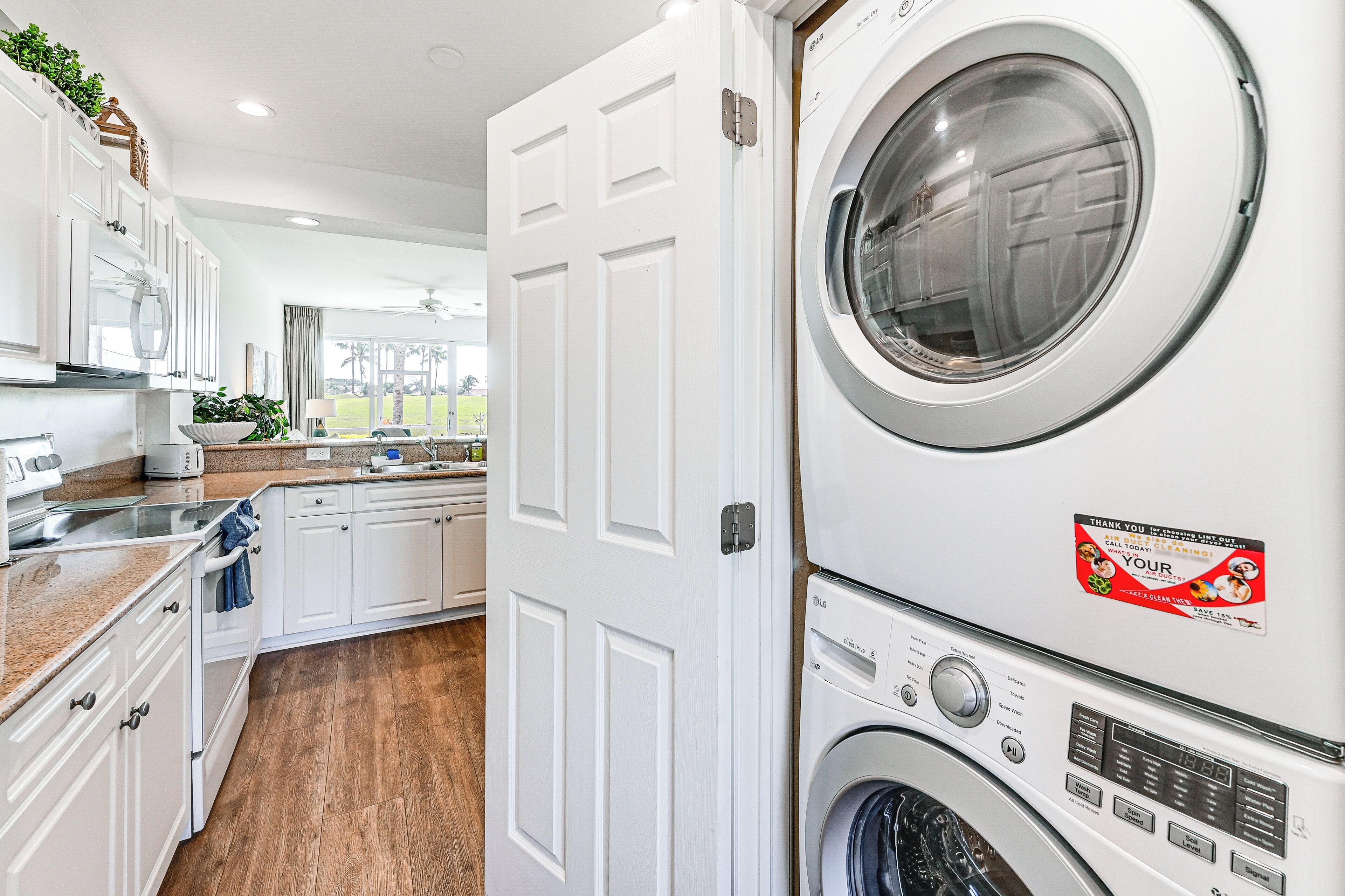 A laundry room with stacked washers and dryers, white cabinetry, and a view of the outside.