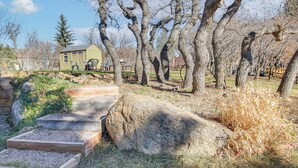 A rustic outdoor setting with a wooden bench, a large rock, and a yellow building in the background. - Private Hot Tub, 4 Mi to Usafa: Cozy Apartment! (Colorado Springs)