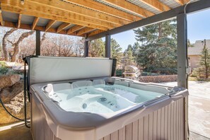 Un bain à remous sous une pergola en bois, avec vue sur les arbres et une maison en arrière-plan.