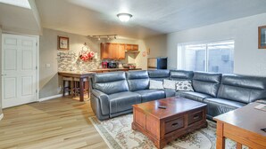 A living room with a sectional sofa, a wooden coffee table, and a kitchen area with wooden cabinets and a refrigerator. - Private Hot Tub, 4 Mi to Usafa: Cozy Apartment! (Colorado Springs)