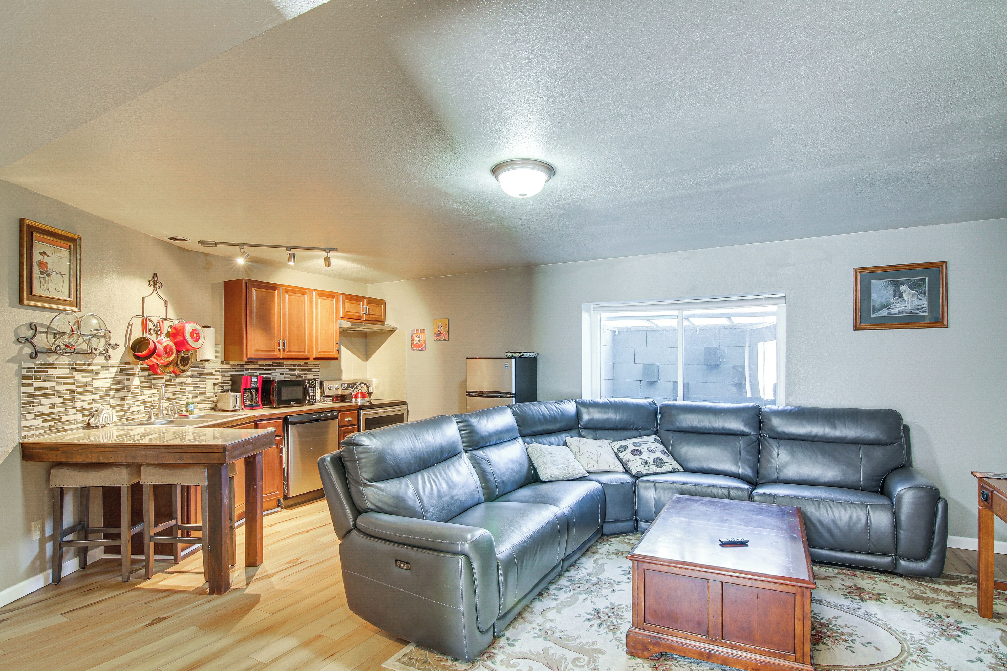A spacious living room with a leather sectional sofa, a wooden coffee table, and a kitchen area with wooden cabinets and a tiled backsplash.