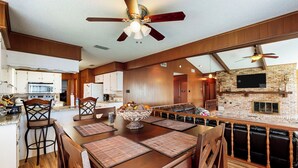 A spacious kitchen with wooden cabinets, a large island with seating, and a stone fireplace. - Laid-back Lake House' w/ Wraparound Deck (Kemp)