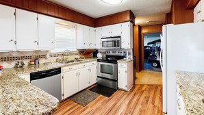 A compact kitchen with white cabinets, a stainless steel oven, a microwave, and a dishwasher. - Laid-back Lake House' w/ Wraparound Deck (Kemp)