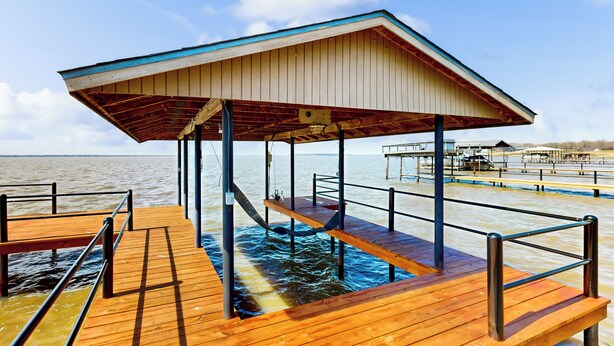 A wooden pier with a covered seating area extending over water, supported by metal beams. - Laid-back Lake House' w/ Wraparound Deck (Kemp)
