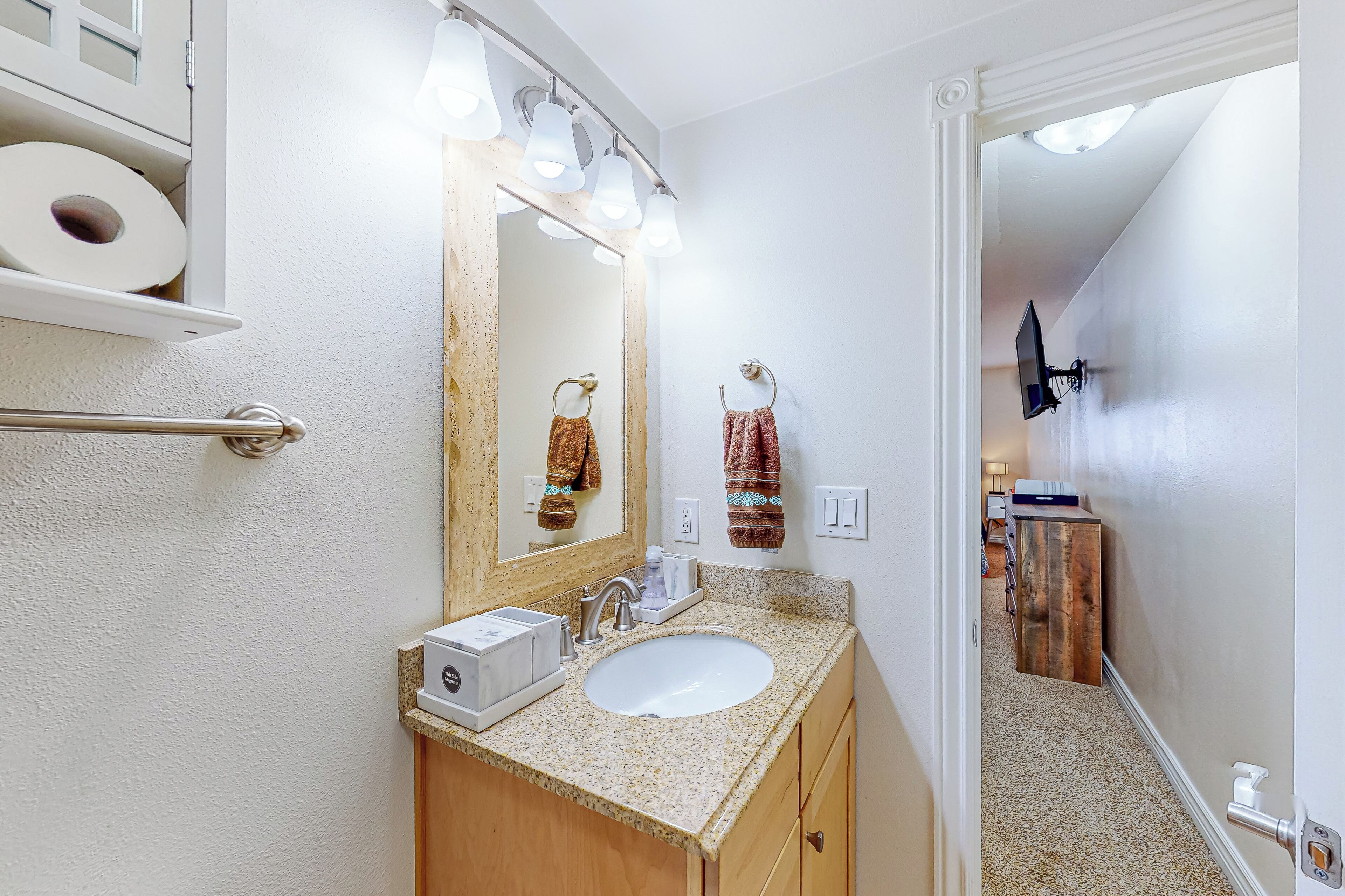 A bathroom with a sink, mirror, towel rack, and a toilet paper holder.