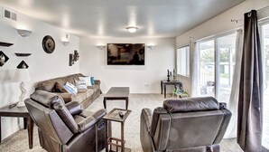 A living room with a brown leather sofa, a coffee table, and a TV mounted on the wall. - Soft Sunsets & Still Water at Flathead Condo (Polson)