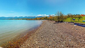 A pebbly lakeshore with a bench and a sign, surrounded by trees and mountains in the background. - Soft Sunsets & Still Water at Flathead Condo (Polson)