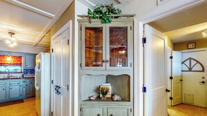 A kitchen with wooden cabinets, a refrigerator, and a decorative shelf with a vase and a small plant. - Get a Wave From it All: Home w/ Private Dock (Pensacola)