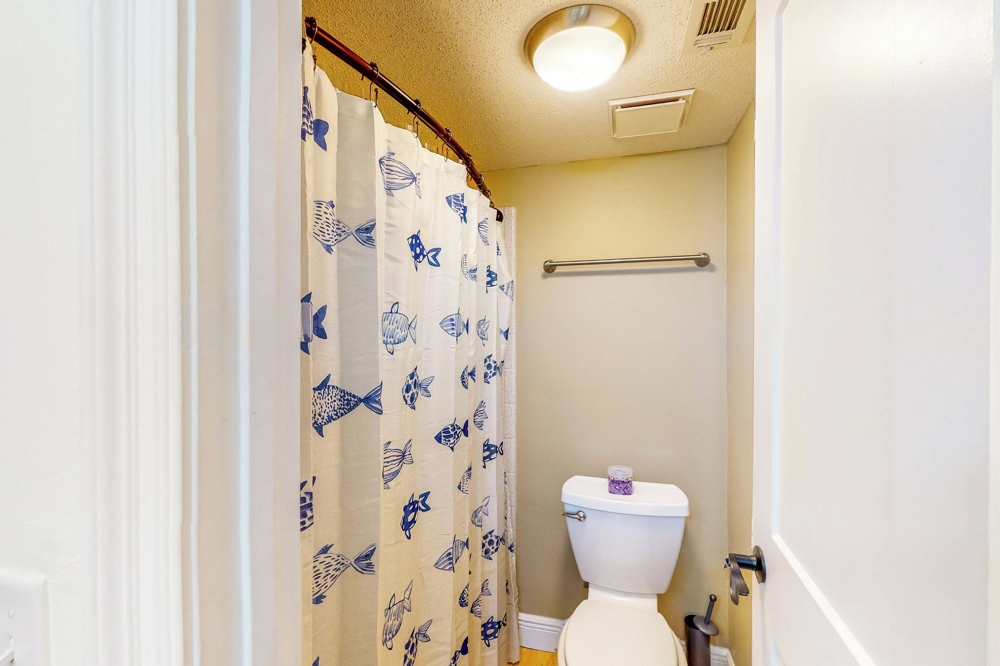 Een badkamer met een toilet, een douchegordijn met een visprint, een handdoekhouder en een lamp aan het plafond.