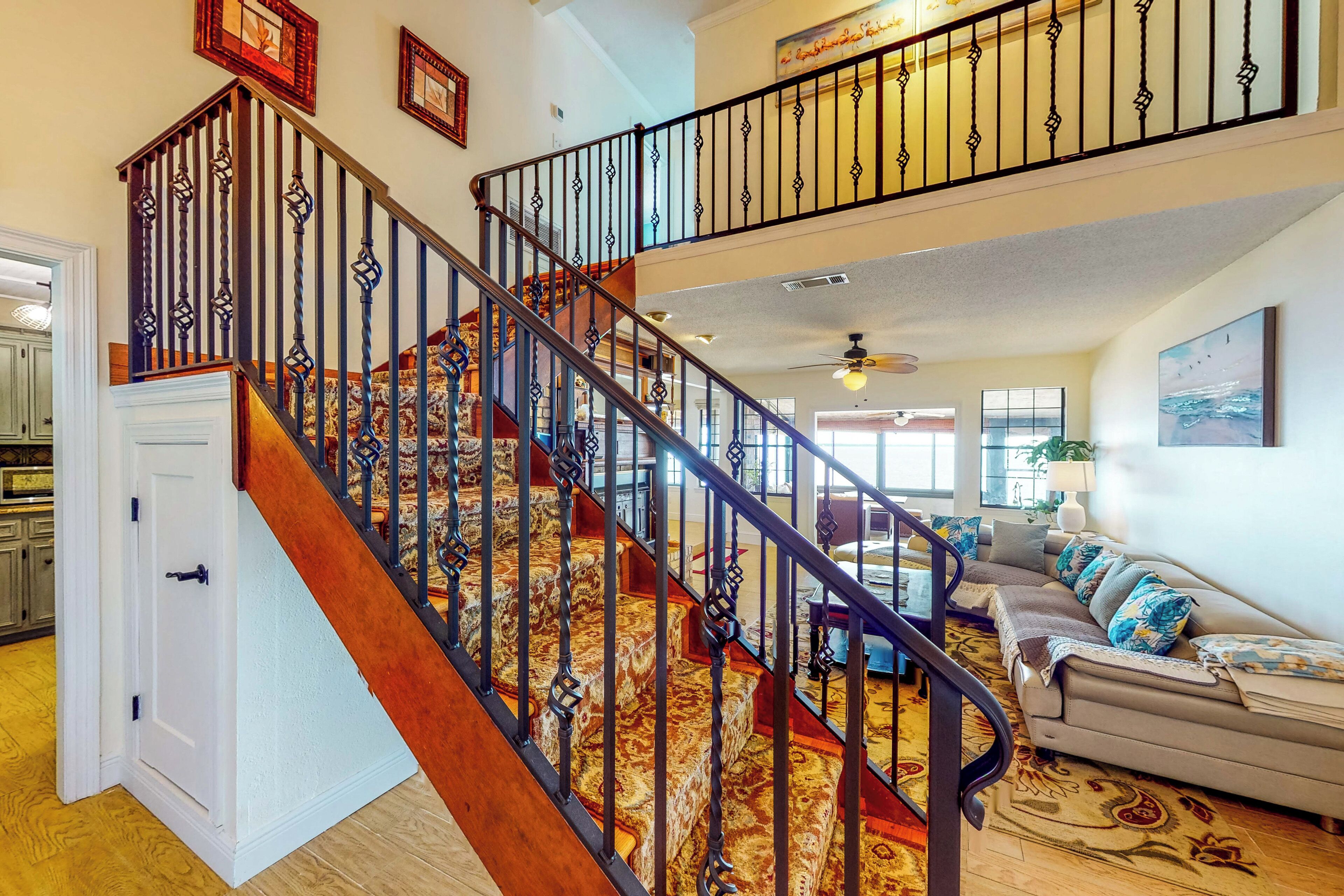 A spacious living area with a wooden staircase, a sofa set, and a patterned rug.