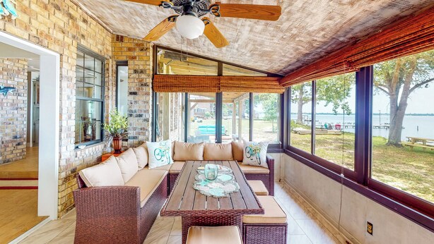 A spacious patio with a wooden table and wicker furniture, large windows offering views of a lake, and a ceiling fan. - Get a Wave From it All: Home w/ Private Dock (Pensacola)