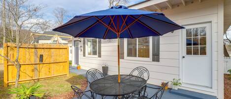 A patio with a round table and chairs, a blue umbrella, and a wooden fence.