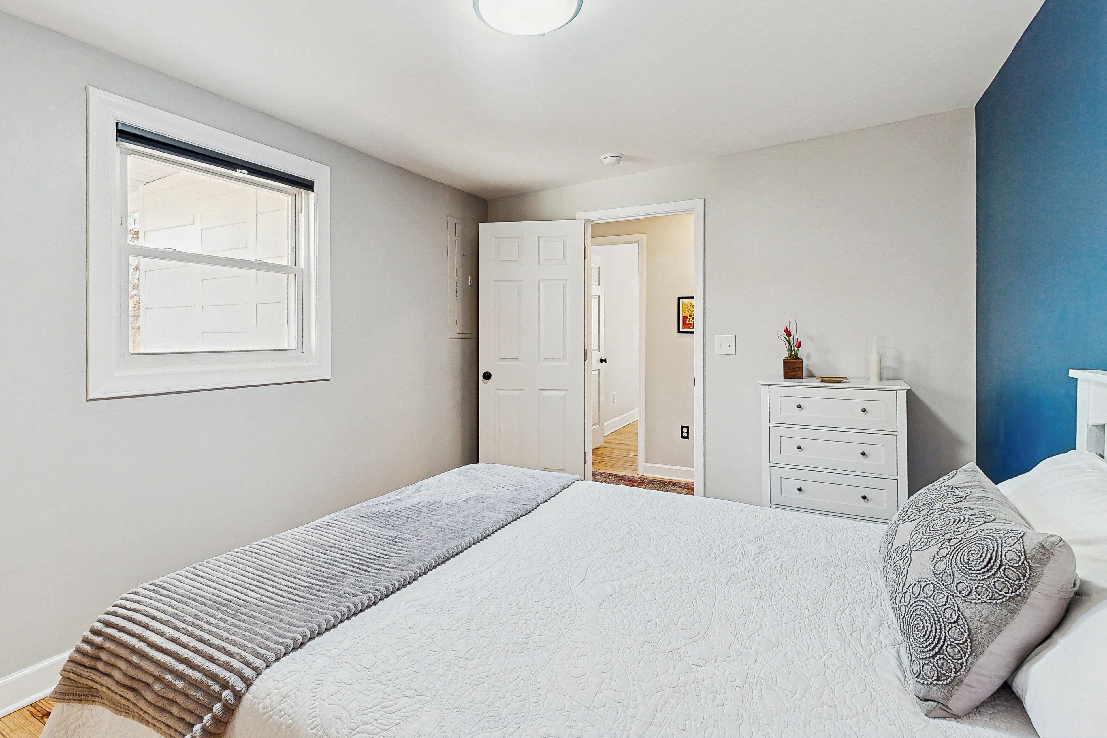 A bedroom with a bed, a dresser, a window, and a door leading to a hallway.