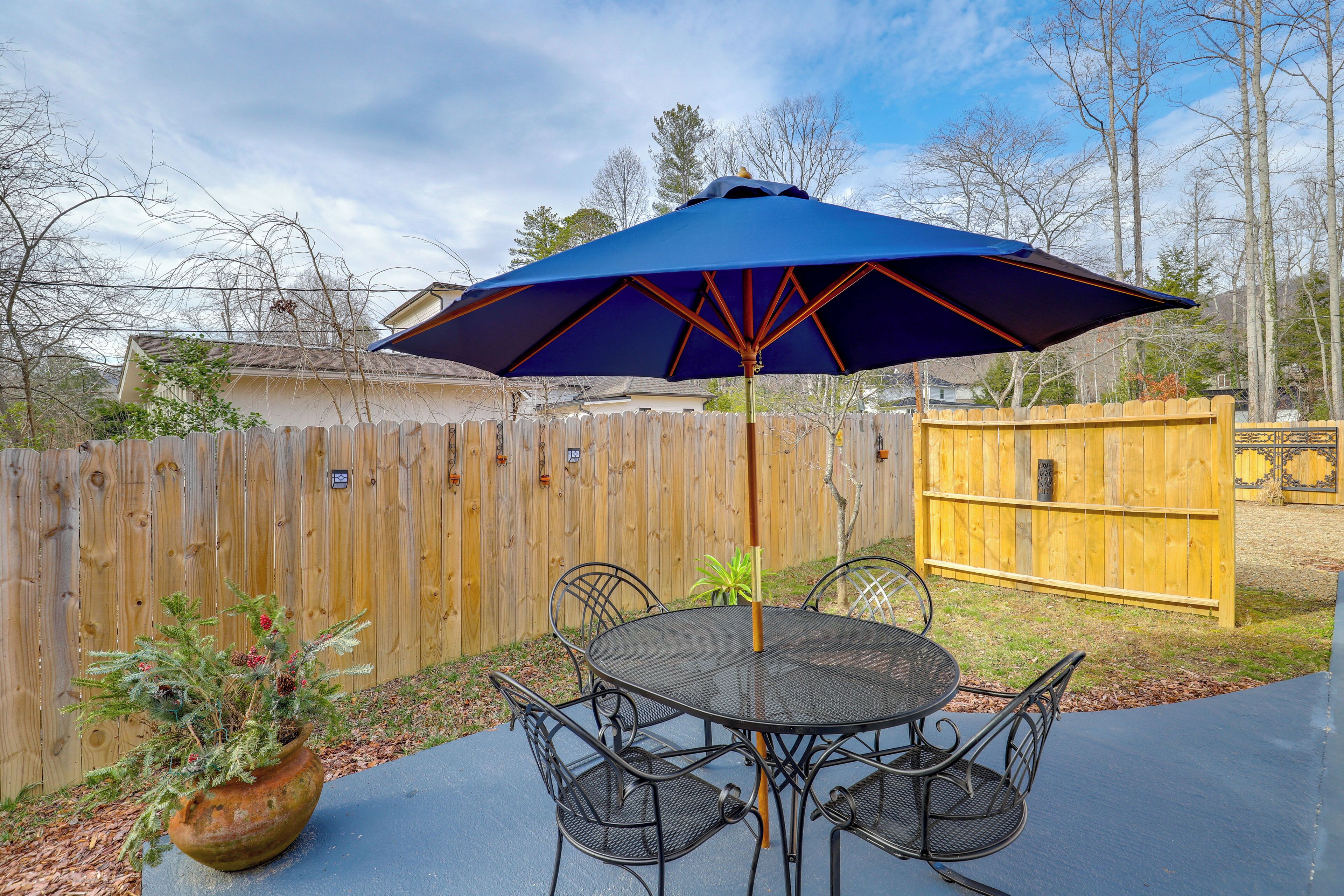 A patio with a round table and chairs, a blue umbrella, and a wooden fence in the background.