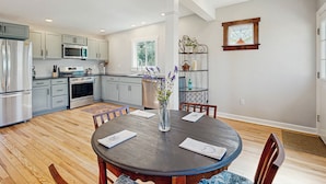 A modern kitchen with grey cabinets, stainless steel appliances, and a dining area with a round table and chairs. - Private Patio & Pond: Serene Black Mountain Escape (Black Mountain)