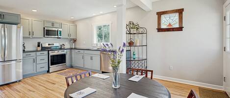 A modern kitchen with grey cabinets, stainless steel appliances, and a dining area with a round table and chairs.