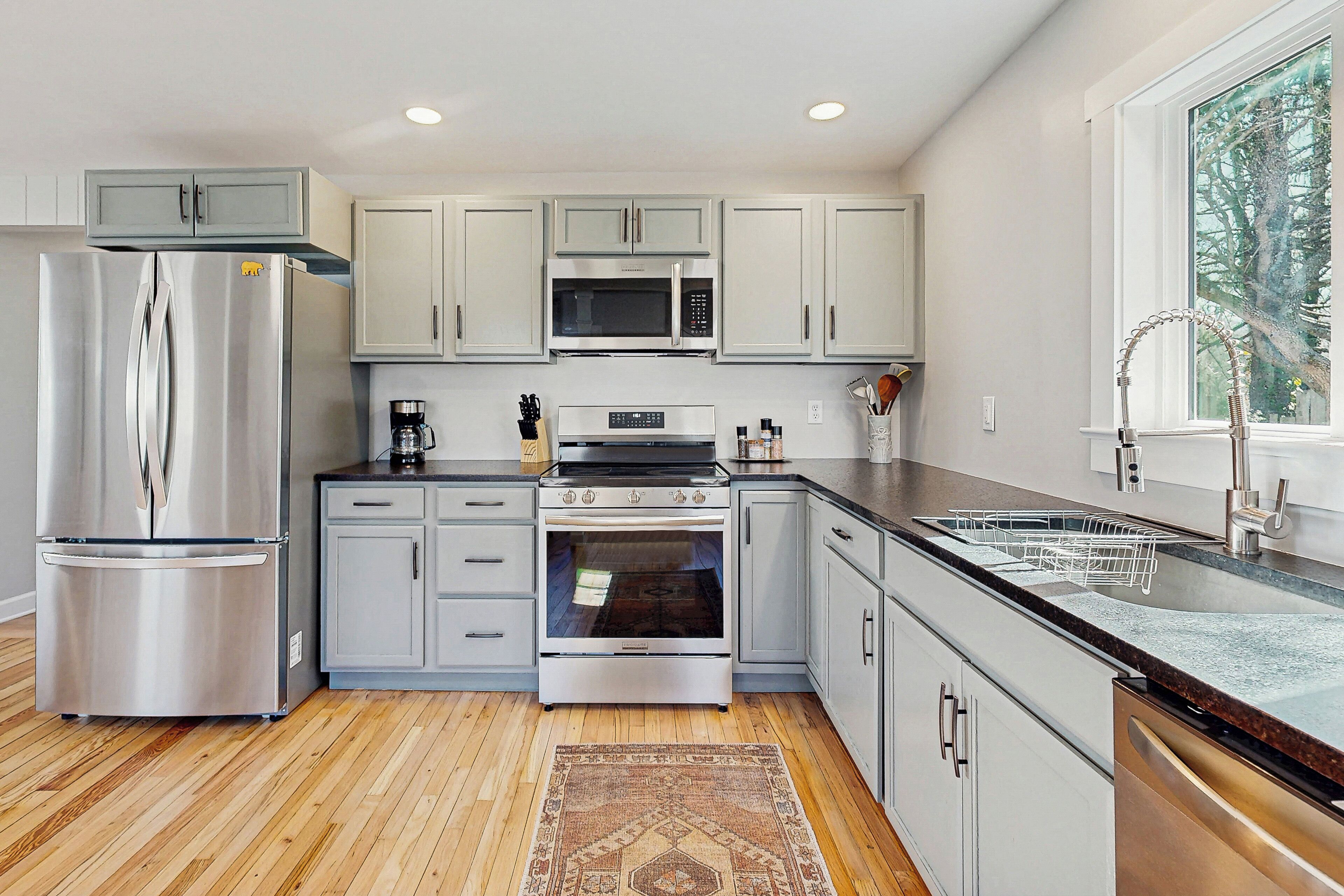 A modern kitchen with stainless steel appliances, light grey cabinets, and a wooden floor.