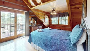 A bedroom with a large bed, wooden ceiling beams, a balcony, and a view of the outdoors. - 3BR Water View, Hot Tub, Fireplace & Balcony (Marshall)