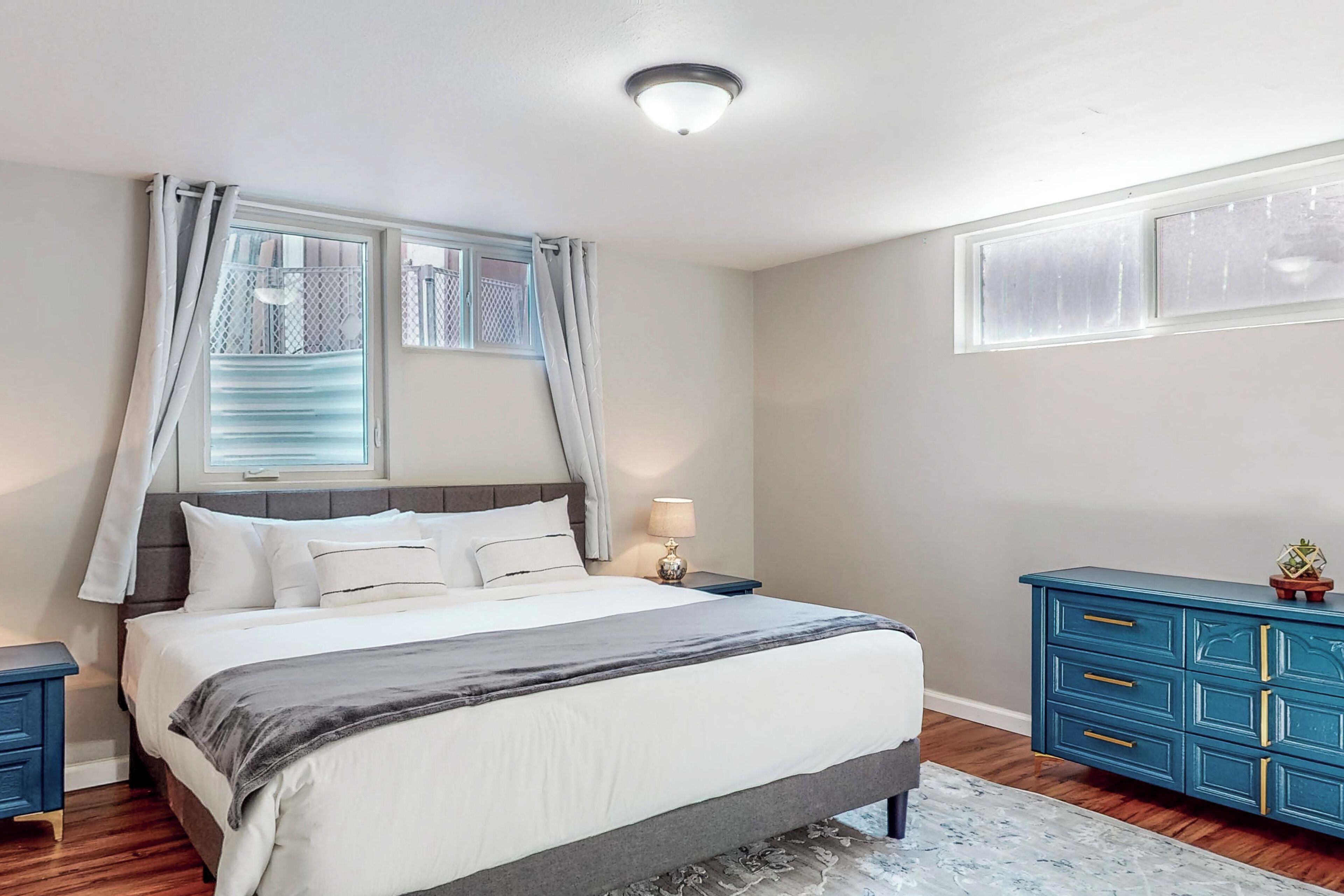A bedroom with a bed, nightstands, a dresser, and a window with curtains.