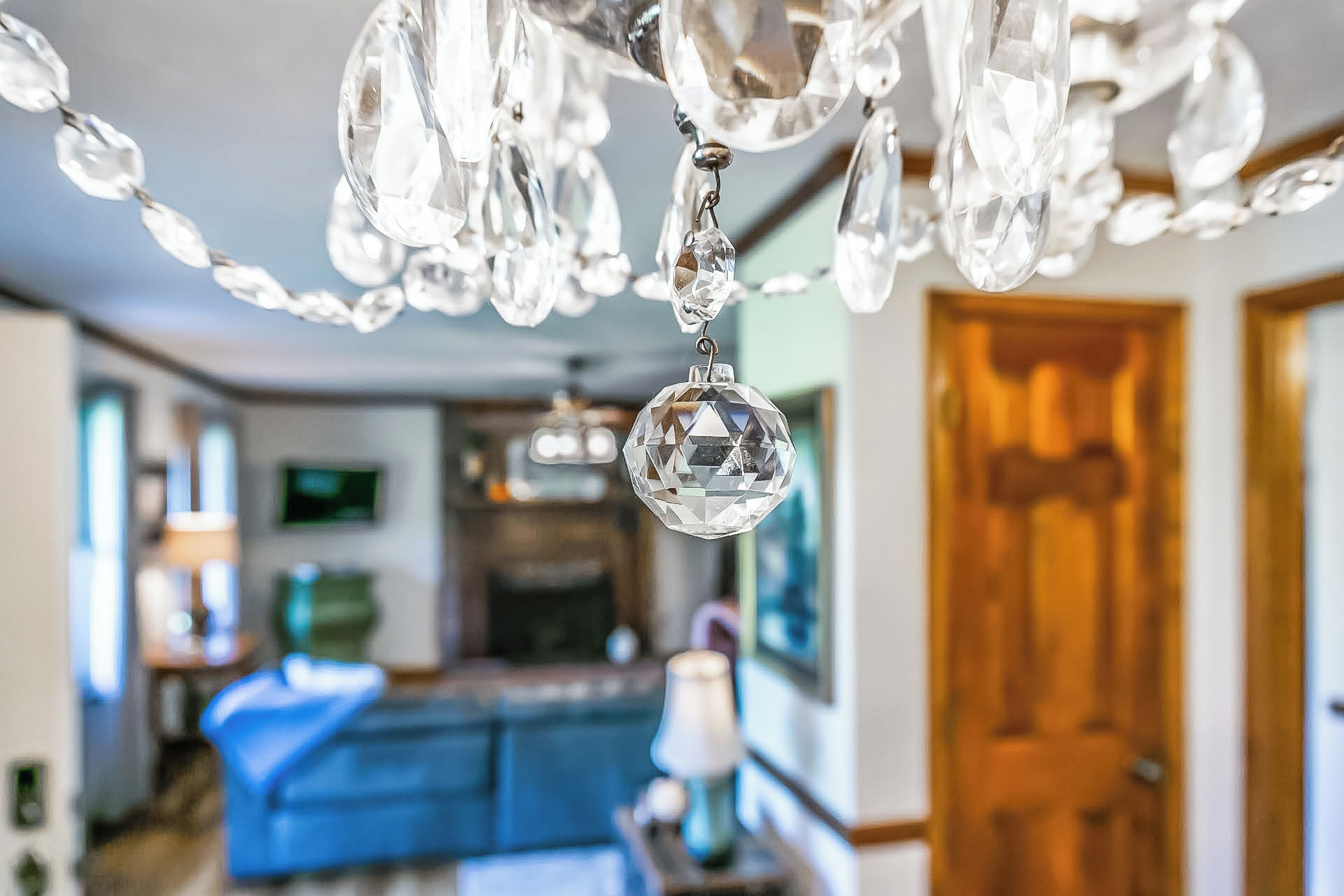 Un candelabro con múltiples detalles de cristal en una habitación que tiene un sofá azul y una puerta de madera.