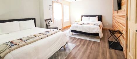 A hotel room with two beds, a ceiling fan, a TV mounted on the wall, and a wooden floor.