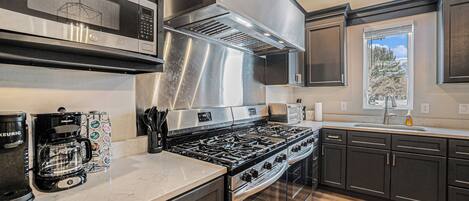 Een moderne keuken met roestvrijstalen apparatuur, donkere kastjes en een groot raam dat voor natuurlijk licht zorgt.