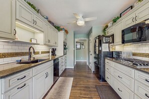 A kitchen with white cabinets, a black microwave, and a stainless steel refrigerator. - Outdoor Spa + Dock! Scenic Norris Lake Retreat (Caryville)