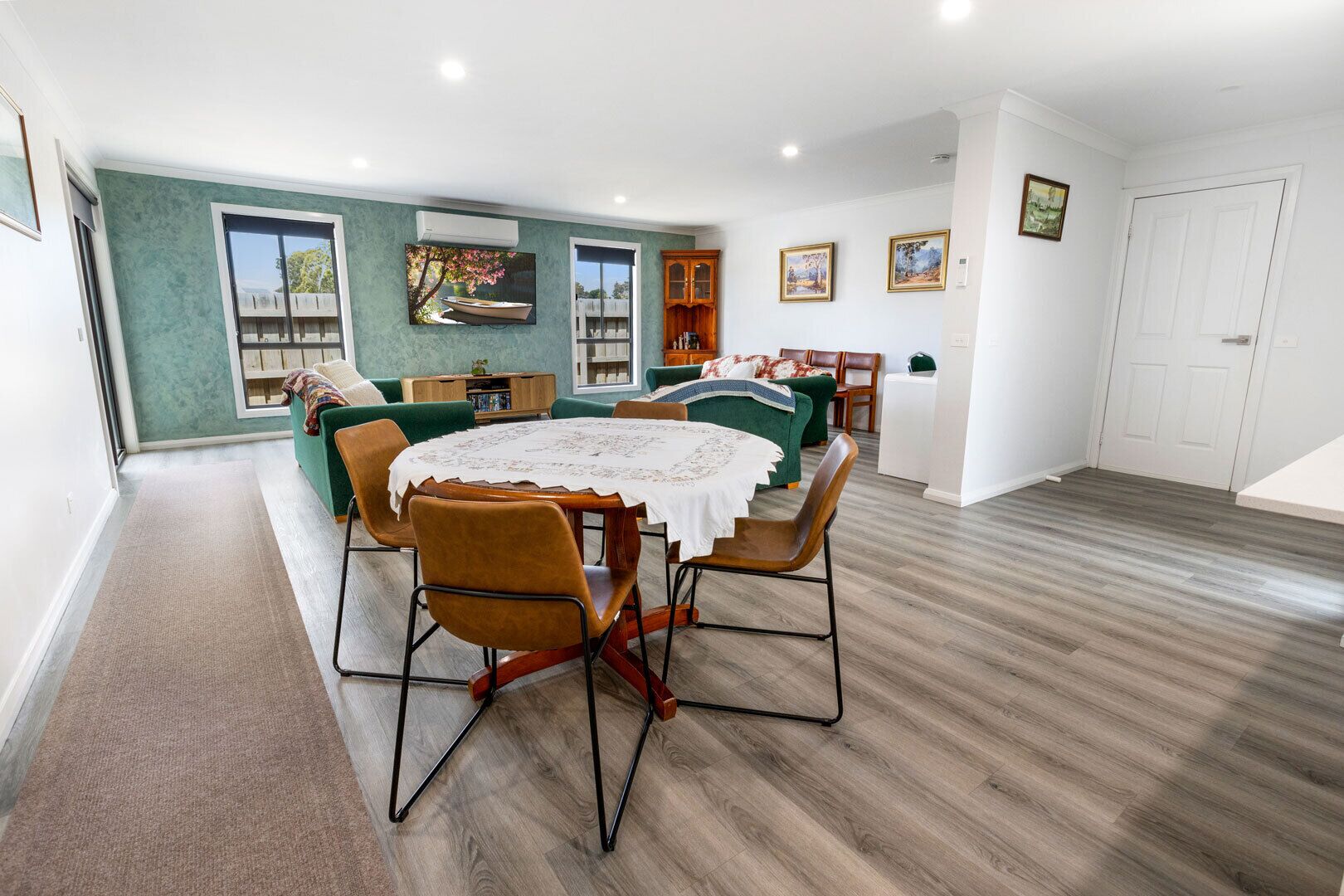 A spacious living room with a dining table, green sofas, and a bookshelf.