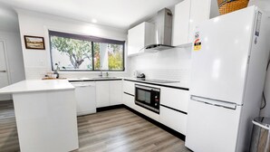 Eine moderne Küche mit weißen Schränken, einem eingebauten Backofen, einem Edelstahl-Kühlschrank und einem Fenster mit Blick auf Bäume.