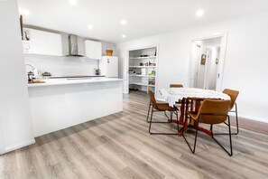 A modern kitchen with white cabinetry, a central island, and a dining area with a table and chairs. - Haylock Haven: Relax, explore, and feel right at home (Paynesville)